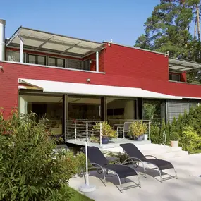 Modernes rotes Holzhaus mit Terrasse, Markise und Garten mit Liegen