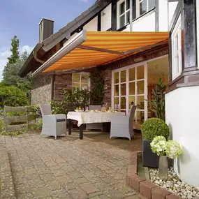 Gelb-orange Markise über Terrasse mit Gartentisch und Stühlen am Haus