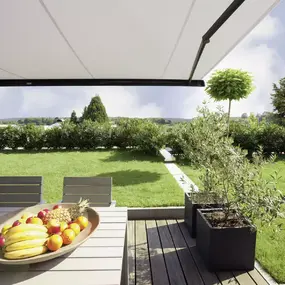 Moderne Terrasse mit Markise, Gartentisch und Obstschale im grünen Garten