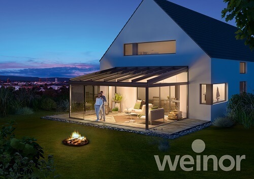 Modernes Einfamilienhaus mit beleuchtetem Wintergarten und Terrasse bei Sonnenuntergang.