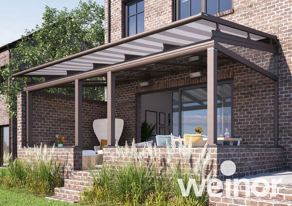 Moderne Terrassenüberdachung aus Glas und Aluminium an einem Backsteinhaus im Garten.