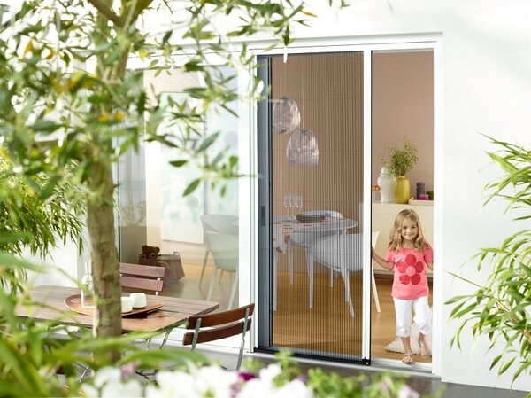 Ein Insektenschutz-Plissee an einer Terrassentür mit spielendem Kind im Sommergarten.