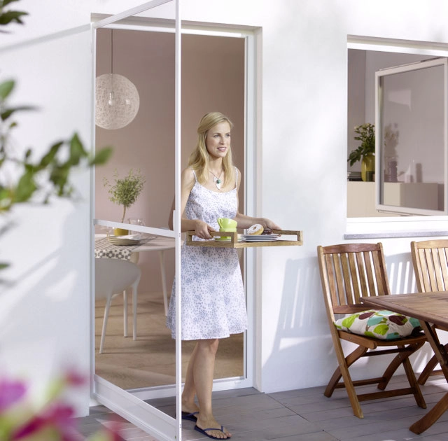 Frau trägt Frühstückstablett durch Terrassentür auf sonnigen Balkon