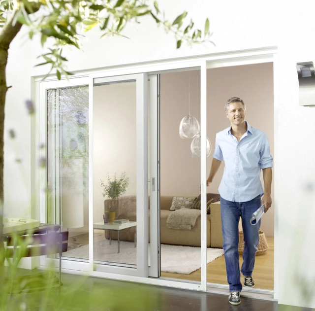 Mann öffnet moderne Schiebetür zur Terrasse, helles Wohnzimmer dahinter