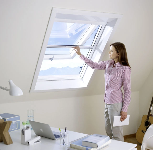 Frau öffnet Dachfenster im Homeoffice, Tageslicht und Lüftung im Raum